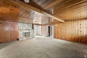 Unfurnished living room featuring wooden ceiling, beam ceiling, and a stone fireplace