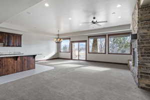 Unfurnished living room featuring light carpet, a fireplace, and ceiling fan with notable chandelier