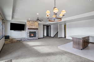 Unfurnished living room with a raised ceiling, ceiling fan with notable chandelier, light colored carpet, and a brick fireplace