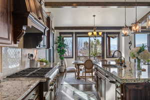 Kitchen featuring light stone countertops, sink, stainless steel appliances, an inviting chandelier, and decorative light fixtures