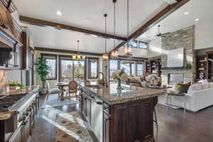 Kitchen with ceiling fan with notable chandelier, a kitchen island with sink, sink, pendant lighting, and a fireplace