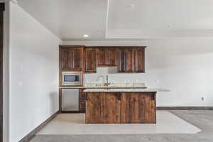 Kitchen featuring dark brown cabinets, a center island, stainless steel microwave, and fridge