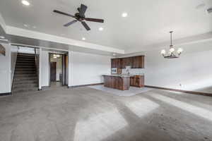 Unfurnished living room featuring ceiling fan with notable chandelier and light colored carpet