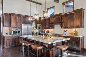 Kitchen featuring dark brown cabinetry, a high ceiling, an island with sink, decorative light fixtures, and appliances with stainless steel finishes