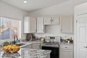 Kitchen with lofted ceiling, white cabinetry, stainless steel electric stove, and light stone counters