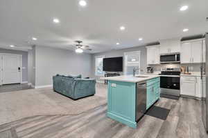 Kitchen with ceiling fan, white cabinets, appliances with stainless steel finishes, and a center island with sink