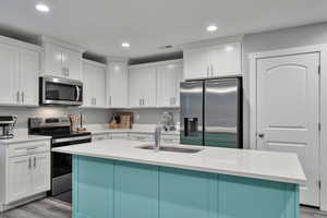 Kitchen featuring hardwood / wood-style flooring, appliances with stainless steel finishes, a kitchen island with sink, white cabinets, and sink