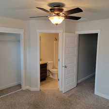 Unfurnished bedroom with light colored carpet, a closet, ceiling fan, and ensuite bathroom