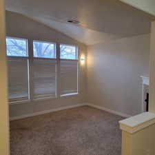 Carpeted empty room with a textured ceiling and vaulted ceiling