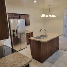 Kitchen featuring dark brown cabinetry, stainless steel refrigerator with ice dispenser, sink, hanging light fixtures, and light colored carpet