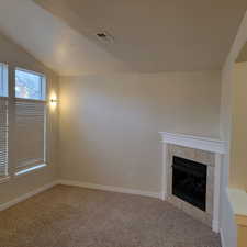 Unfurnished living room with vaulted ceiling, a tile fireplace, a textured ceiling, and carpet flooring