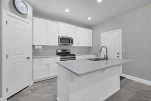 Kitchen featuring appliances with stainless steel finishes, a kitchen island with sink, sink, and white cabinets