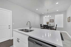 Kitchen with sink, white cabinetry, light stone counters, decorative light fixtures, and dishwasher