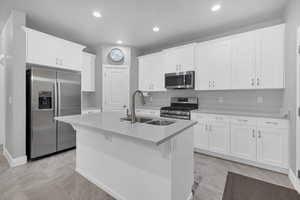 Kitchen featuring an island with sink, white cabinetry, sink, a kitchen bar, and stainless steel appliances