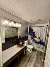 Full bathroom with toilet, shower / bath combo, wood-type flooring, a textured ceiling, and vanity