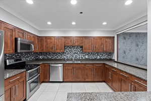 Kitchen featuring appliances with stainless steel finishes, tasteful backsplash, dark stone countertops, sink, and light tile patterned flooring