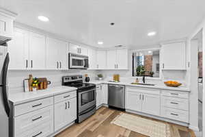 Kitchen featuring stainless steel appliances, light hardwood / wood-style flooring, white cabinetry, and sink