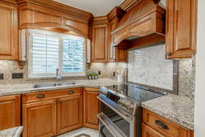 Kitchen with tasteful backsplash, premium range hood, double oven range, sink, and light stone countertops