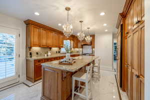 Kitchen featuring a kitchen bar, an inviting chandelier, an island with sink, hanging light fixtures, and light stone counters