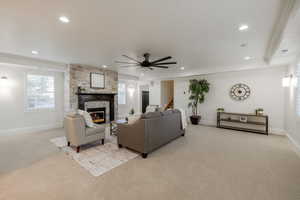 Carpeted living room with ceiling fan, a wealth of natural light, ornamental molding, and a stone fireplace