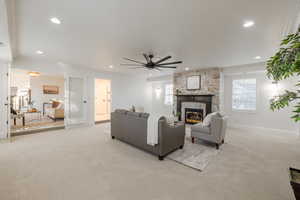 Living room with ceiling fan, light colored carpet, a stone fireplace, and ornamental molding