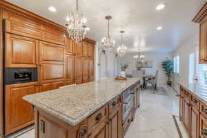 Kitchen with light stone countertops, hanging light fixtures, a center island, and a notable chandelier