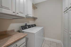 Clothes washing area featuring light tile patterned floors, cabinets, and washer and dryer