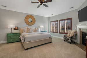 Carpeted bedroom featuring ceiling fan and a tiled fireplace