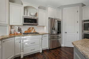 Kitchen with backsplash, light stone countertops, dark wood-type flooring, stainless steel appliances, and white cabinets