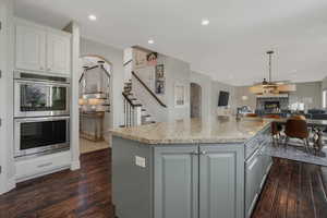 Kitchen with a center island with sink, a stone fireplace, stainless steel double oven, dark hardwood / wood-style floors, and white cabinets