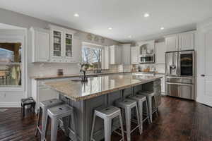 Kitchen featuring stainless steel appliances, dark hardwood / wood-style flooring, light stone countertops, a kitchen island, and white cabinets