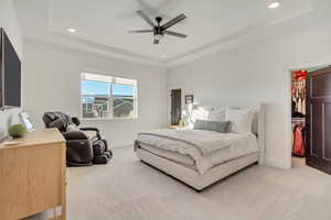 Carpeted bedroom with ceiling fan, a walk in closet, a closet, and a raised ceiling