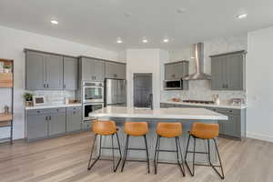 Kitchen with a breakfast bar area, appliances with stainless steel finishes, gray cabinetry, sink, and wall chimney range hood