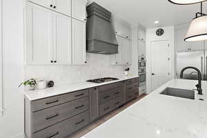 Kitchen with stainless steel appliances, custom range hood, pendant lighting, light stone counters, and sink