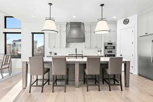 Kitchen featuring hanging light fixtures, a center island with sink, custom range hood, and stainless steel appliances