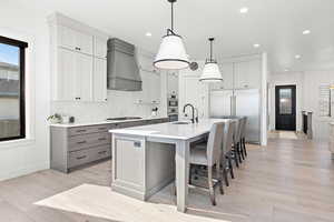 Kitchen featuring a spacious island, pendant lighting, custom exhaust hood, sink, and stainless steel appliances