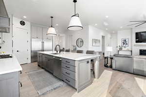 Kitchen featuring decorative light fixtures, appliances with stainless steel finishes, an island with sink, and gray cabinets