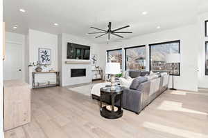 Living room with ceiling fan, light wood-type flooring, and a large fireplace