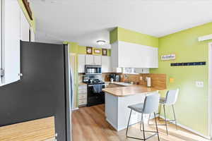 Kitchen with appliances with stainless steel finishes, white cabinetry, a kitchen breakfast bar, backsplash, and kitchen peninsula