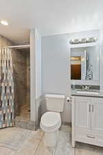 Bathroom with toilet, a shower with shower curtain, tile patterned flooring, and vanity