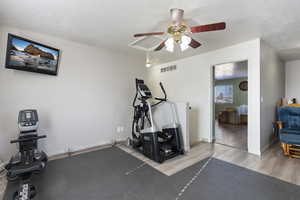 Exercise area featuring a textured ceiling, ceiling fan, and light hardwood / wood-style floors