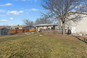 Rear view of property featuring a wooden deck, a storage unit, and a yard