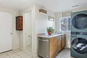 Washroom with light tile patterned floors, stacked washer and dryer, and sink