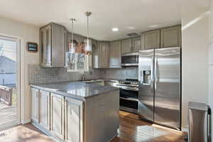 Kitchen featuring stainless steel appliances, backsplash, dark hardwood / wood-style floors, decorative light fixtures, and dark stone countertops