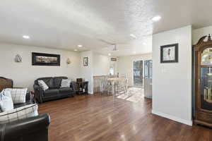 Living room featuring a textured ceiling, ceiling fan, and dark hardwood / wood-style floors