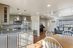 Kitchen featuring stainless steel appliances, decorative backsplash, hanging light fixtures, dark hardwood / wood-style floors, and ceiling fan