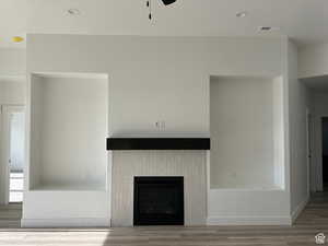 Unfurnished living room with ceiling fan, wood-type flooring, and a fireplace