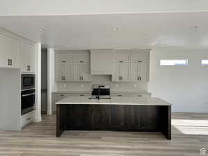 Kitchen with light stone countertops, sink, stainless steel oven, a center island with sink, and built in microwave