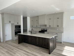 Kitchen featuring sink, wall chimney range hood, appliances with stainless steel finishes, and a kitchen island with sink