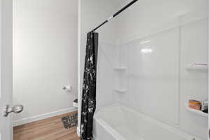 Bathroom with shower / bathtub combination with curtain, toilet, and wood-type flooring